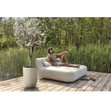 Buitenscène met bloeiende boom in plantenbak en man op een ligbed met kussens