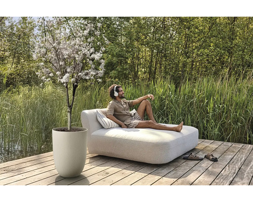 Buitenscène met bloeiende boom in plantenbak en man op een ligbed met kussens