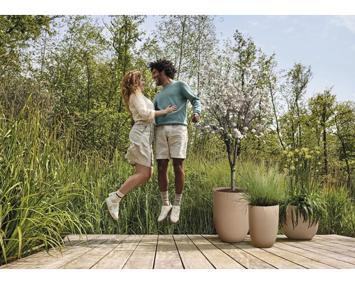 Een paar springt op een houten terras met plantenbakken in een tuin.