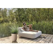 Scene met man op een tuinbank met kussens, potplant en schoenen op een houten terras aan een meer