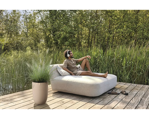 Scene met man op een tuinbank met kussens, potplant en schoenen op een houten terras aan een meer