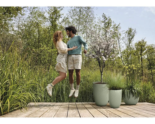 Een stel springt op een houten terras naast drie plantenbakken.