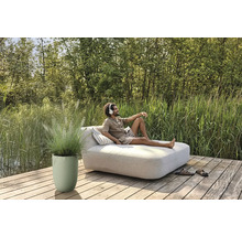 Man ontspant met een koptelefoon op een tuinbank op een houten terras naast een plantenbak met siergras.