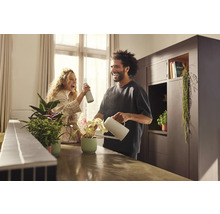 Man geeft kamerplant water met gieter, terwijl vrouw plantenspuit gebruikt