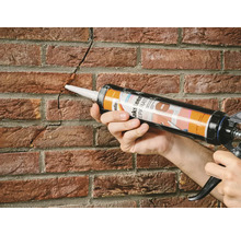 Persoon repareert met een kitpistool een scheur in een bakstenen muur.