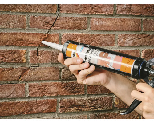 Persoon repareert met een kitpistool een scheur in een bakstenen muur.