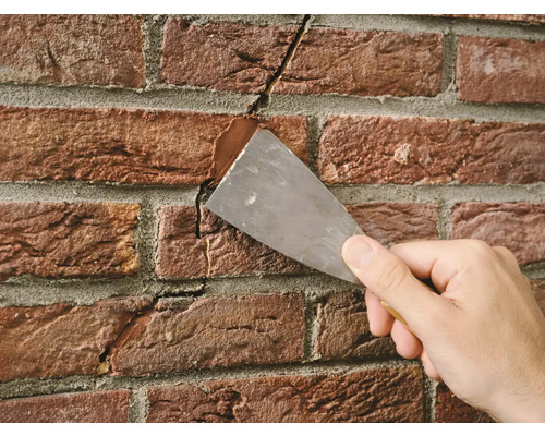 Een scheur in een bakstenen muur wordt gevuld met een plamuurmes en voegmassa.