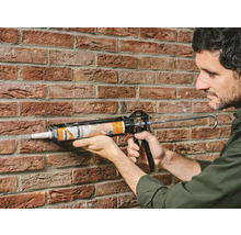 Man gebruikt een kitpistool om een voeg op een bakstenen muur af te dichten.