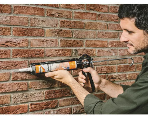 Man gebruikt een kitpistool om een voeg op een bakstenen muur af te dichten.