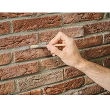 Een hand die met een penseel voegen op een bakstenen muur reinigt.