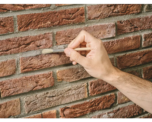 Een hand die met een penseel voegen op een bakstenen muur reinigt.