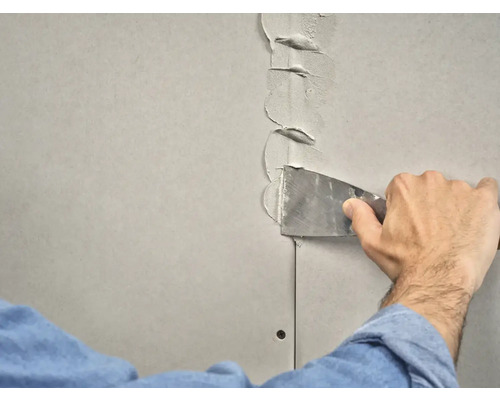 Iemand vult een gipsplaatvoeg met een plamuurmes.