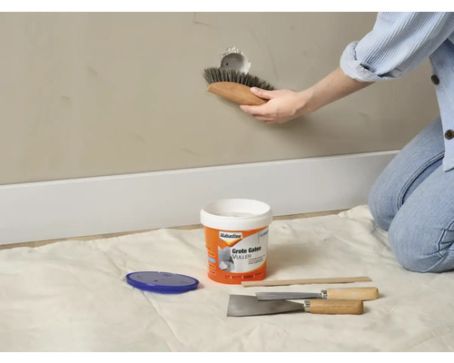 Persoon repareert een gat in de muur met vulmiddel en gereedschap