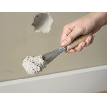 Hand met plamuurmes en vulmiddel voor het repareren van een gat in de muur.