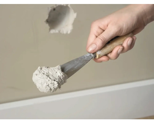 Hand met plamuurmes en vulmiddel voor het repareren van een gat in de muur.