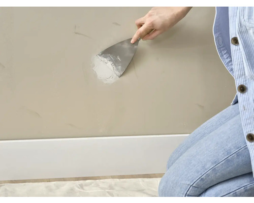 Een persoon egaliseert vulmiddel op een muur met een plamuurmes.