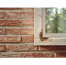 Beschadigd houten raamkozijn naast een bakstenen muur.