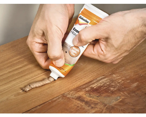 Een vakman vult met een tube houtrotvuller een voeg in een houten vloer.