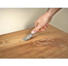 Hand verwijdert plamuur van een houten tafel met een plamuurmes