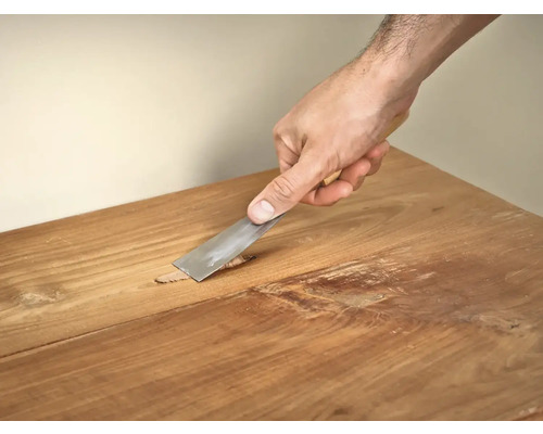 Hand verwijdert plamuur van een houten tafel met een plamuurmes