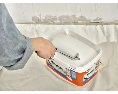 Een persoon dompelt een verfroller in een emmer muurverf van Alabastine Muurglad.