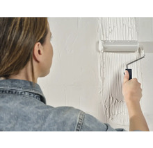 Een vrouw schildert een muur met een verfroller.