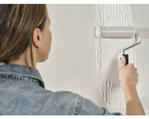 Een vrouw schildert een muur met een verfroller.