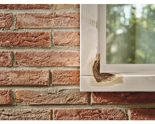 Beschadigd houten raam naast een bakstenen muur.