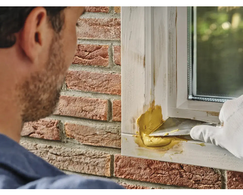 Een man brengt plamuur aan op een raamkozijn met een plamuurmes.