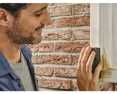 Man schuurt een houten raam met een schuurblok.