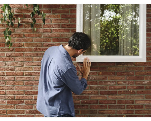 Man inspecteert een raam in een bakstenen muur.