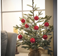 Versierde kleine kerstboom met rode ballen in juten zak