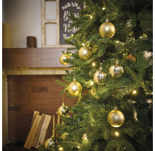 Versierde kerstboom met gouden en zilveren kerstballen en lichtjes in een woonkamer met open haard