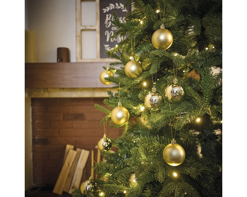 Versierde kerstboom met gouden en zilveren kerstballen en lichtjes in een woonkamer met open haard