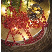 Decoratie met rode kralenketting, dennentakken, lichtsnoer en dennenappels op een bord