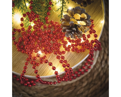 Decoratie met rode kralenketting, dennentakken, lichtsnoer en dennenappels op een bord