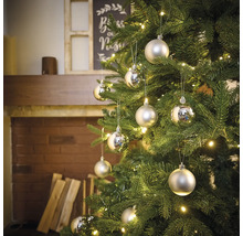 Versierde kerstboom met zilverkleurige ballen en verlichting in een woonkamersfeer