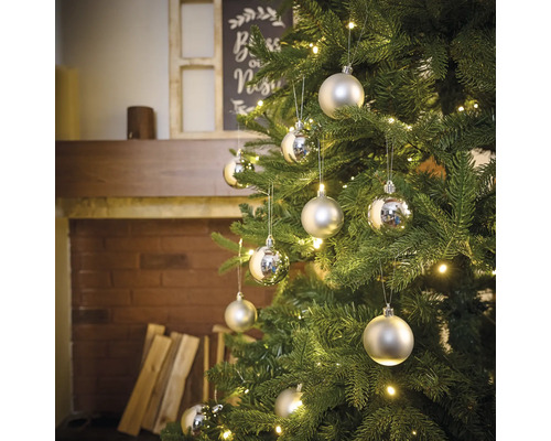 Versierde kerstboom met zilverkleurige ballen en verlichting in een woonkamersfeer