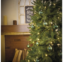 Versierde kerstboom met verlichting en ballen naast een open haard