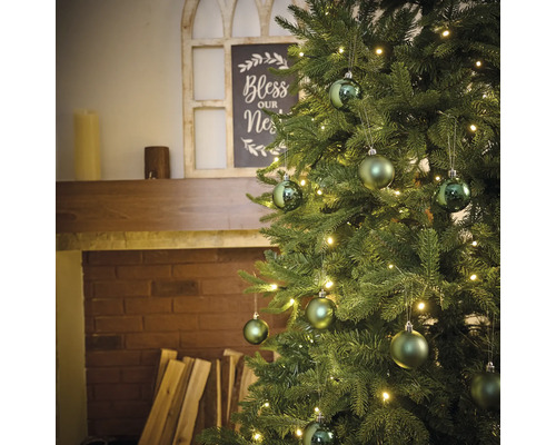 Versierde kerstboom met verlichting en ballen naast een open haard