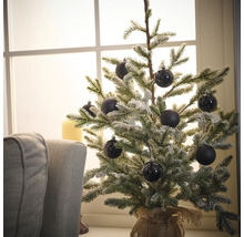 Decoratieve, besneeuwde kerstboom met zwarte ballen op een tafel bij een raam