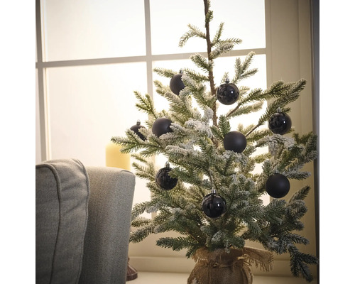 Decoratieve, besneeuwde kerstboom met zwarte ballen op een tafel bij een raam