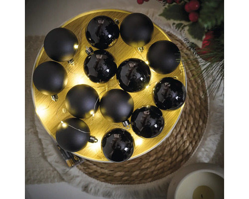 Arrangement van zwarte kerstballen met matte en glanzende afwerking, aangevuld met een lichtslinger op een rond dienblad
