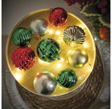 Decoratieve kerstballen in groen, zilver en rood op een versierde tafel.
