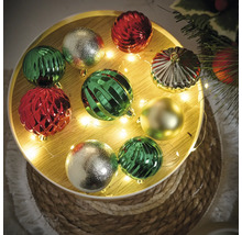 Decoratieve kerstballen in groen, rood en goud op een rond dienblad met lichtjes.