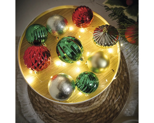 Decoratieve kerstballen in groen, rood en goud op een rond dienblad met lichtjes.