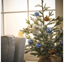 Versierde kleine kerstboom met kerstballen voor een raam
