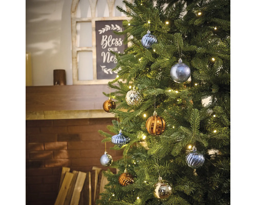 Versierde kerstboom met verschillende kerstballen en een lichtsnoer in de woonkamer.
