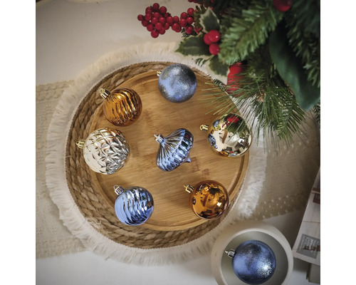 Veelkleurige kerstballen op een houten dienblad naast een kerstboom.