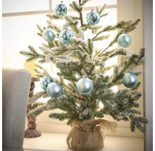 Decoratieve kleine kerstboom met kerstballen in juten zak op vensterbank